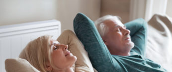 couple senior dans leur canapé avec un radiateur basse consommation Aterno derrière eux
