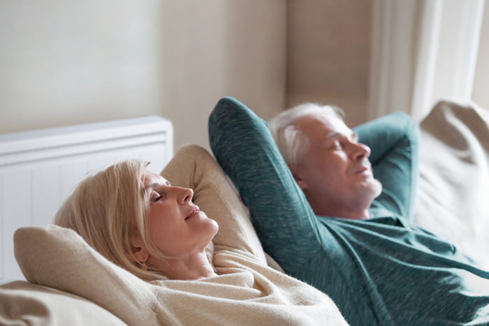 couple senior dans leur canapé avec un radiateur basse consommation Aterno derrière eux